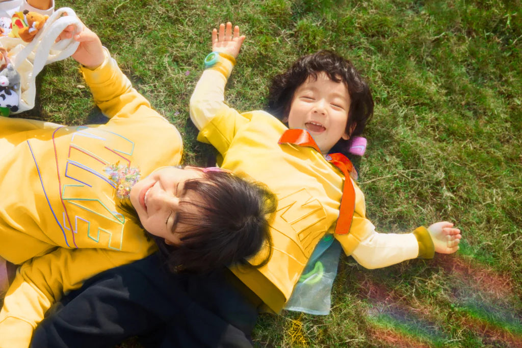 Two children in yellow outfits lying on grass with a rainbow in the background
